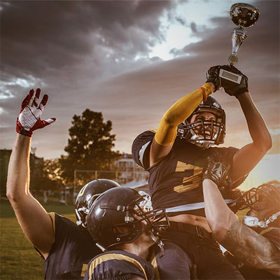 A football team carries a player holding a trophy in the air.