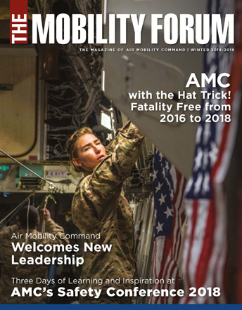Dressed in camouflage fatigues, a person adjusts an American flag banner on the cover of an issue of The Mobility Forum magazine published for Air Mobility Command.  
