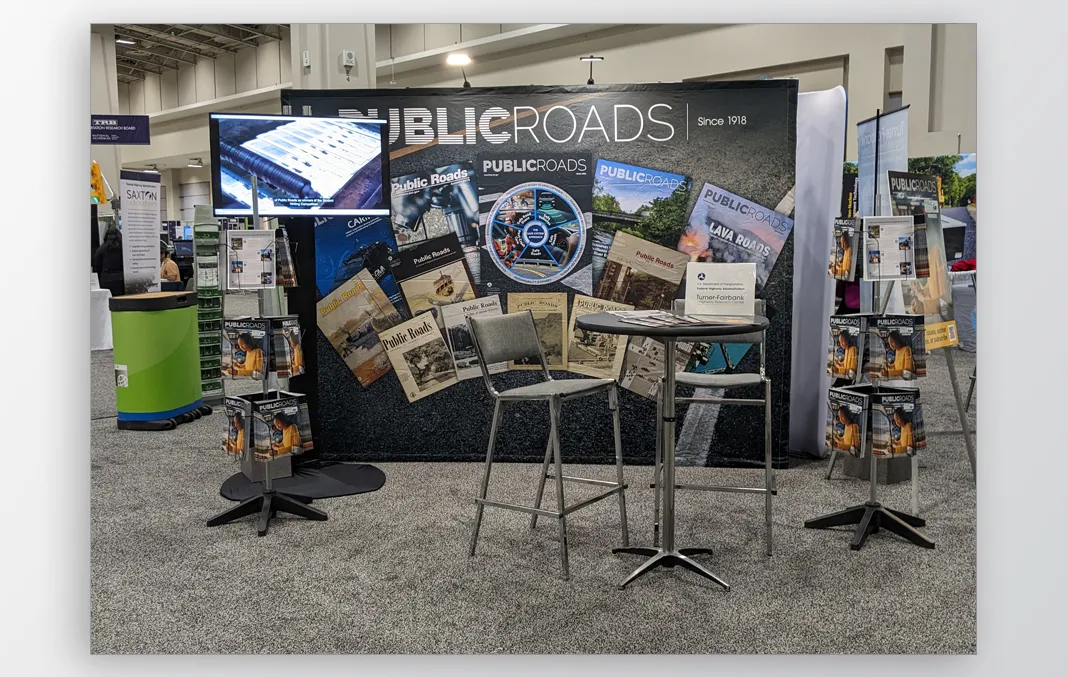 Trade show booth display featuring a banner for Public Roads and displays of printed materials beside a chair and table with printed materials splayed on top of it.